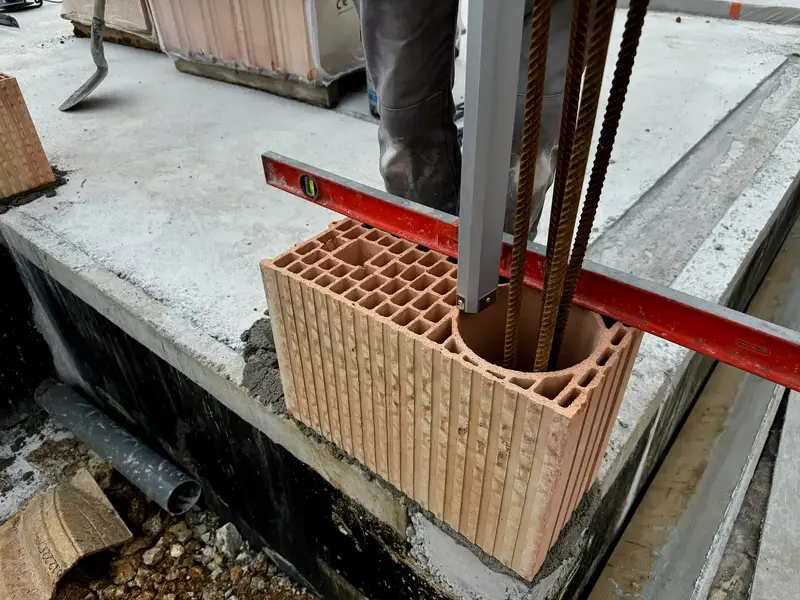 Première brique monomur posée d’aplomb sur l’arase étanchée