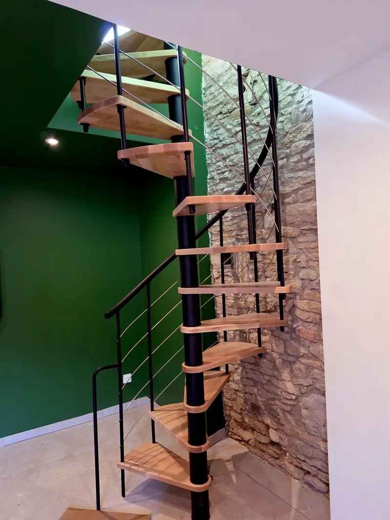 Escalier hélicoïdal en métal et bois posé contre un mur en pierre conservé