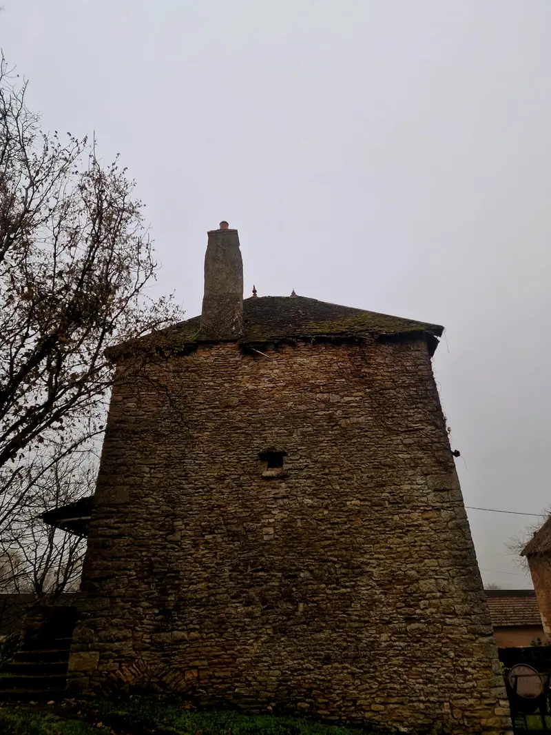 Le corps du moulin en contre-plongée, toiture à quatre pentes couverte de mousse, souche de cheminée en pierre, une seule ouverture